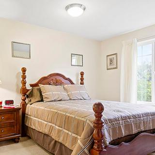 A cozy bedroom with a wooden bed and matching nightstand, complemented by neutral decor and plenty of natural light from a large window.