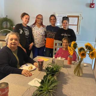 A group of people gathered around a dining table with sunflowers.