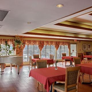 A cozy restaurant interior featuring tables with red tablecloths and a piano, set against a backdrop of large windows.