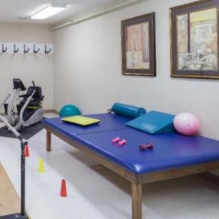 A physical therapy room equipped with exercise mats, balls, weights, and a stationary bike.