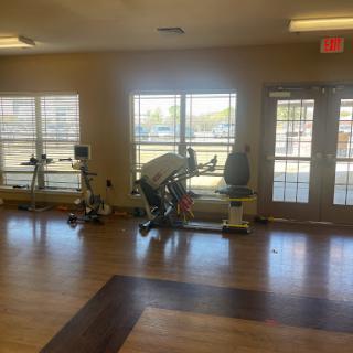 A bright and spacious gym area featuring various exercise equipment with large windows allowing ample natural light.