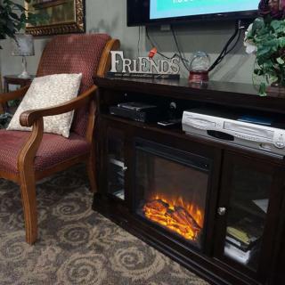 A cozy living room with an upholstered chair, electric fireplace, and a television.