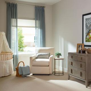 A cozy and well-lit nursery with a crib, armchair, and dresser.