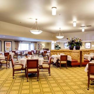 A spacious and elegantly decorated dining room with tables, chairs, and booths arranged neatly under warm lighting.