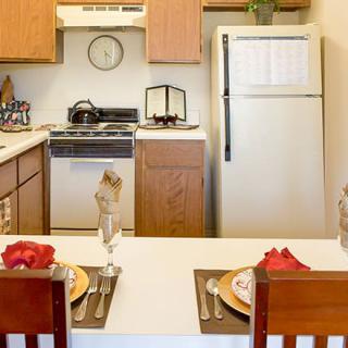 A cozy kitchen with a dining area set for two, featuring a stove and refrigerator.