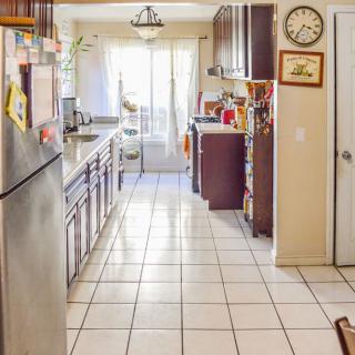 A spacious kitchen with tiled floors and wooden cabinets, illuminated by natural daylight.