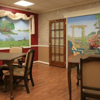 A cozy dining area with tables and chairs, featuring decorative wall murals and wood flooring.