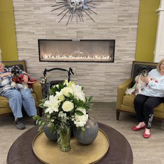 A cozy lounge area featuring a fireplace and a floral arrangement, where two seniors enjoy their time together.