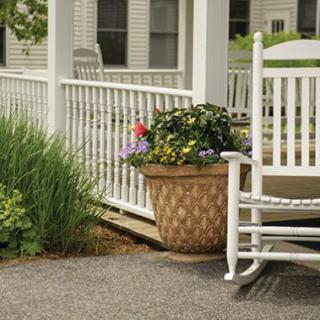 A cozy porch with a white rocking chair next to a potted plant filled with colorful flowers.