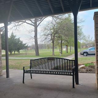 A serene view of a bench under a shelter, surrounded by trees and open space.