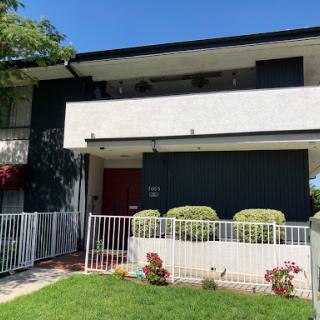A two-story residential building with a modern design, featuring a fenced lawn and clear blue skies.