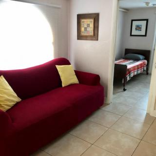 A cozy living space featuring a red sofa with yellow pillows, adjacent to a bedroom with a neatly made bed.
