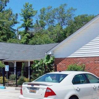 A white car parked near a brick building surrounded by trees under a clear blue sky.