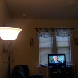 A cozy living room with a lit lamp, television, and curtained windows.