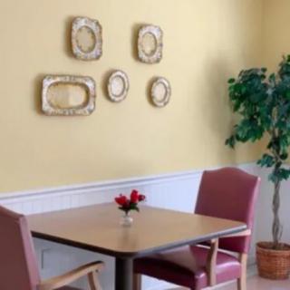 A cozy dining area with a table, two chairs, decorative wall frames, and a potted plant.