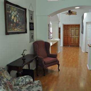 A cozy hallway with wooden flooring, featuring an armchair and a side table under a decorative painting.