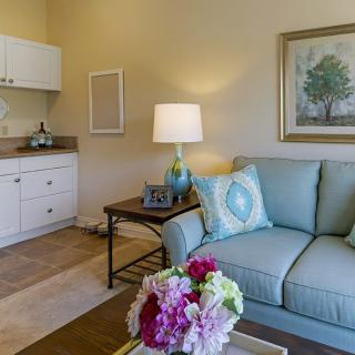 A cozy living room with a light blue sofa and decorative cushions, featuring a lamp on a side table and colorful flowers adding vibrancy to the space.