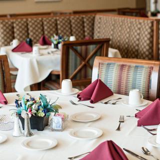 An elegantly set dining table with maroon napkins and a floral centerpiece in a restaurant.