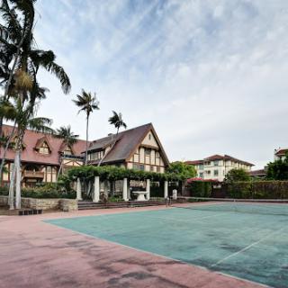 A beautiful mansion with a tennis court surrounded by palm trees.