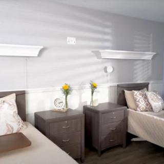 A modern, minimalist bedroom featuring two beds with nightstands, decorated with vases of yellow flowers and wall-mounted shelves.