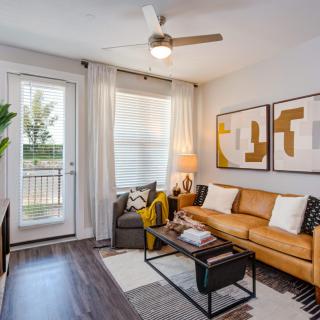 A modern living room with a leather sofa, abstract artwork on the wall, and ample natural light coming through glass doors.