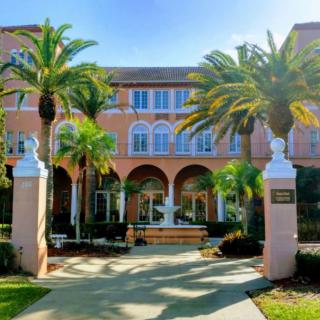 A historic building with palm trees and a fountain at the entrance on a sunny day.