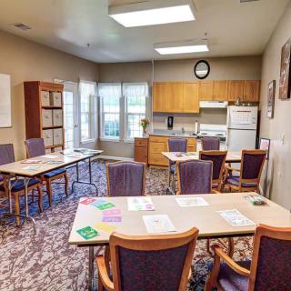 A classroom with multiple tables and chairs, featuring a kitchen area and bright lighting.