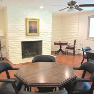 A cozy room featuring a fireplace, a wooden table with chairs, and a ceiling fan.
