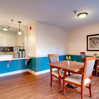 A modern dining area with wooden flooring, featuring tables and chairs, an open kitchen counter, and decorative lighting.