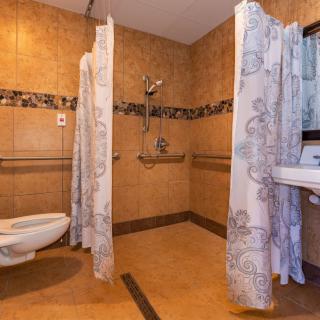 An accessible bathroom with a shower area equipped with curtains, a wall-mounted toilet, and a sink.