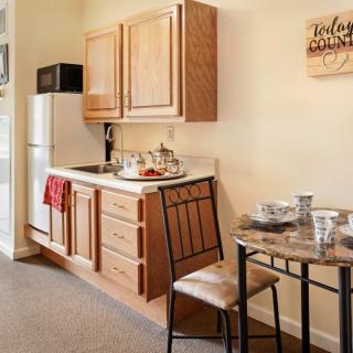 A compact kitchen setup with wooden cabinets, a refrigerator, microwave, and a small dining area for two.
