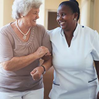 A caregiver and an elderly woman enjoy a warm moment while walking together.