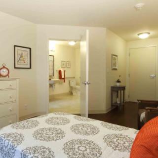 A cozy bedroom interior with a bed, dresser, and an open doorway to a bathroom.