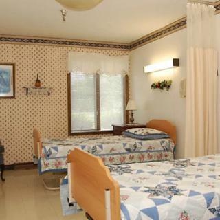 A shared hospital room with two beds separated by a privacy curtain, featuring blue and beige decor.