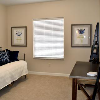 A cozy bedroom with a bed, desk, and framed artwork on the walls.