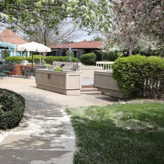 A peaceful garden setting with a pathway leading to an outdoor patio area surrounded by lush greenery and trees in bloom.