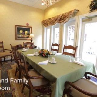 A cozy dining room with a set table and chairs, featuring large windows and a chandelier.