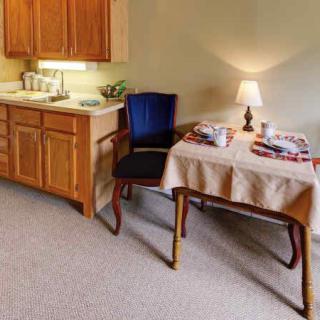 A small kitchen and dining area with a table, lamp, and cabinets.