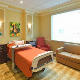A well-lit hospital patient room featuring a bed, seating area, and artwork on the walls.
