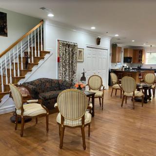 A cozy living room with a seating area and wooden flooring, featuring a staircase and an open kitchen.