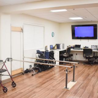 A rehabilitation therapy room equipped with parallel bars, a walker, and workstations for patients.