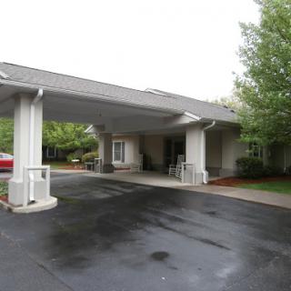A view of the entrance to a building with a covered driveway and surrounding greenery.