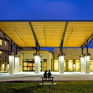 A modern building with a wooden canopy and outdoor seating, illuminated at night.