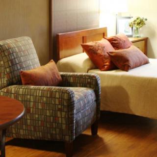 A cozy hotel room featuring an armchair, a bed with multiple pillows, and soft lighting.