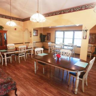 A cozy dining area with several tables and chairs, warm lighting, and wooden flooring.