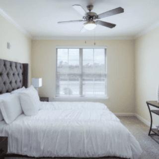 A cozy bedroom with a neatly made bed, a ceiling fan, and natural light from the window.