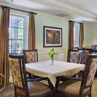 A cozy dining area with a square table and four upholstered chairs, set near windows with brown curtains.