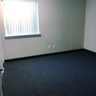 An empty office room with carpet flooring and a window with blinds.