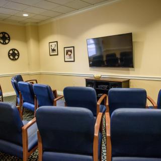 A small conference room with rows of chairs facing a large television on the wall.