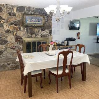 A cozy dining room with a wooden table and chairs, a chandelier above, and a stone fireplace in the background.